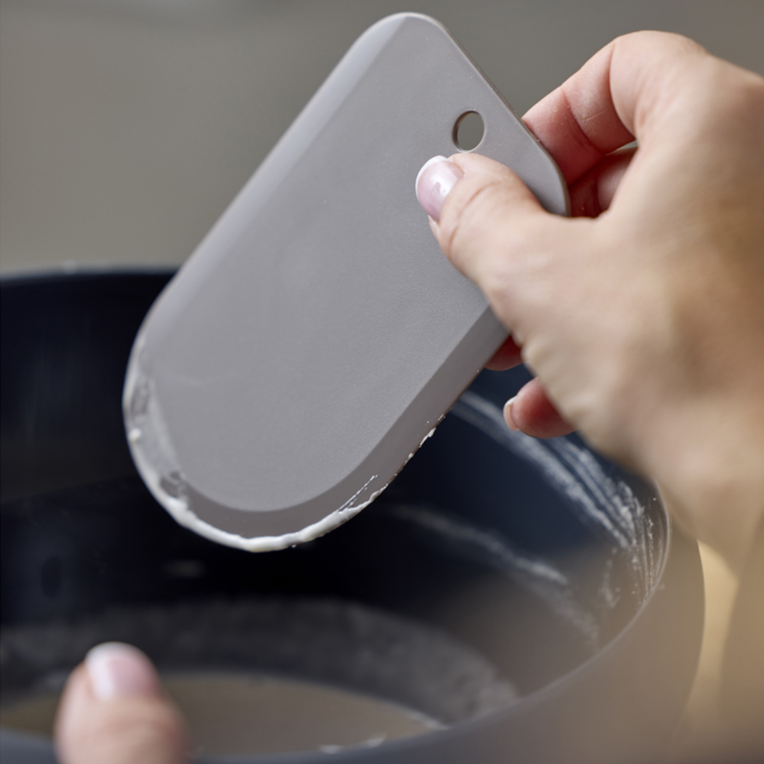 Grå fleksibel dejskraber i plastik bruges til at skrabe en skål ren for dej