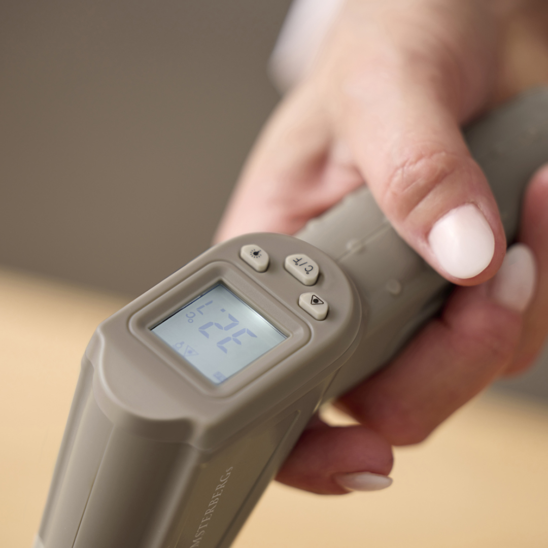 Infrarødt termometer i latte/beige med digitalt display der viser temperatur og tre knapper