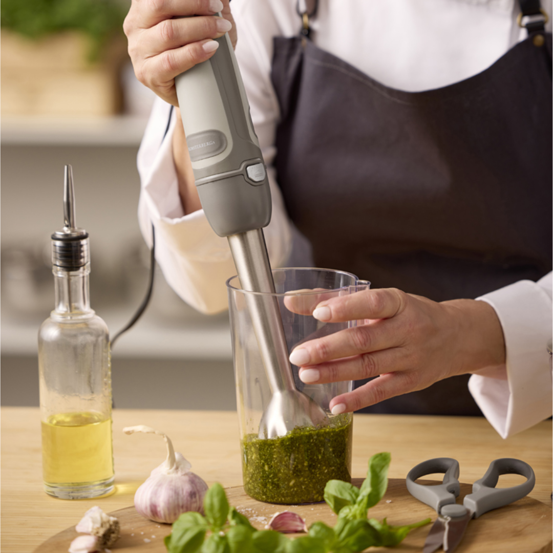 Beige stavblender med rustfrit stålstav bruges til at blende grøn sauce i målebæger