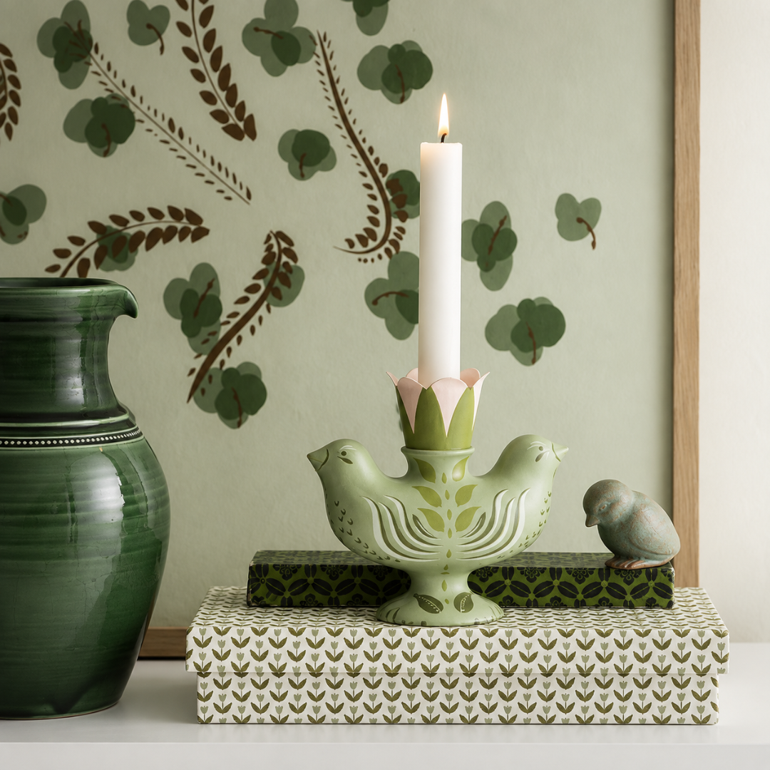 Grøn lysestage i resin med to fugle og lyserød blomsterholder med tændt hvidt lys