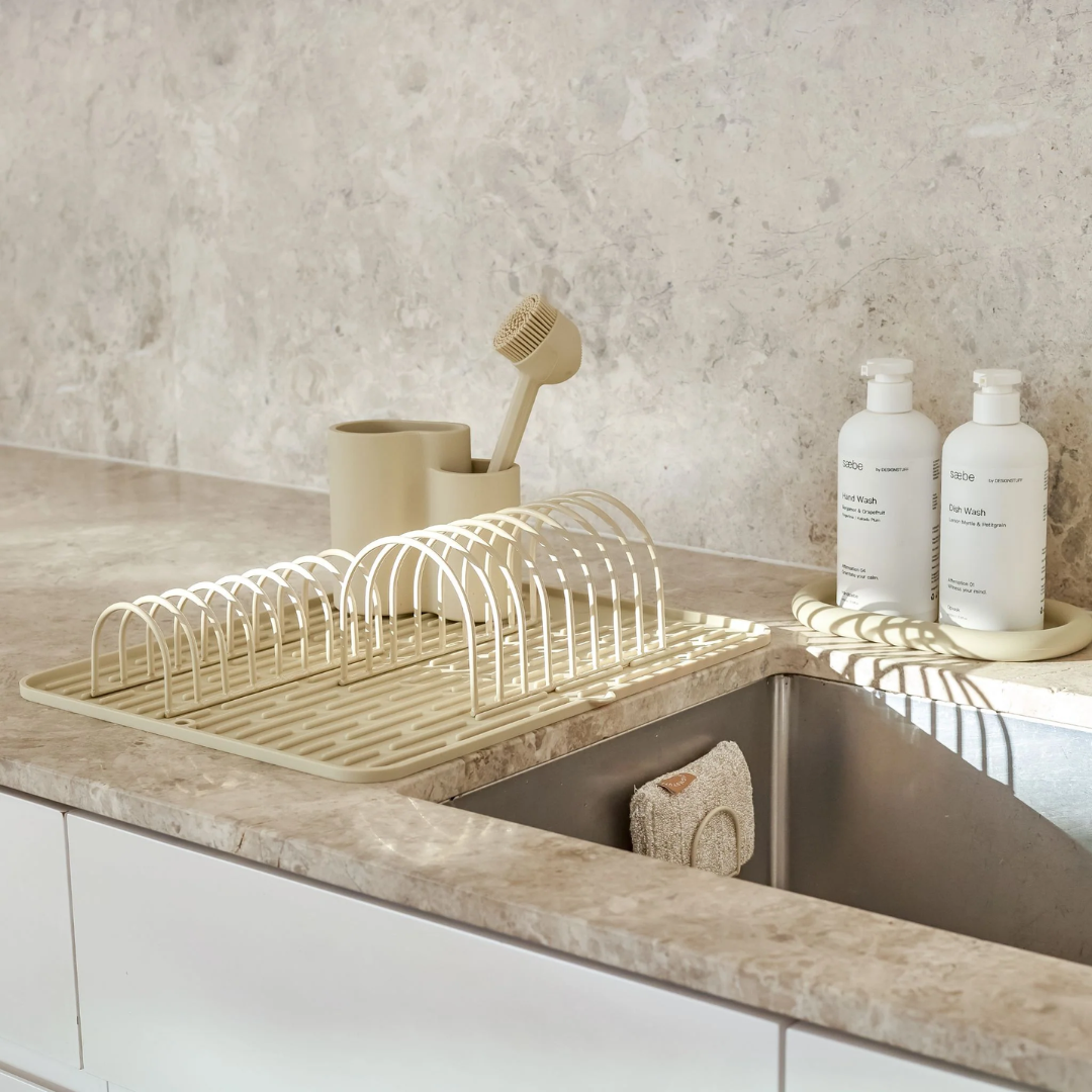 Sandfarvet foldbar silikone opvaskebakke med bueformet stativ placeret på marmorbordplade ved køkkenvask