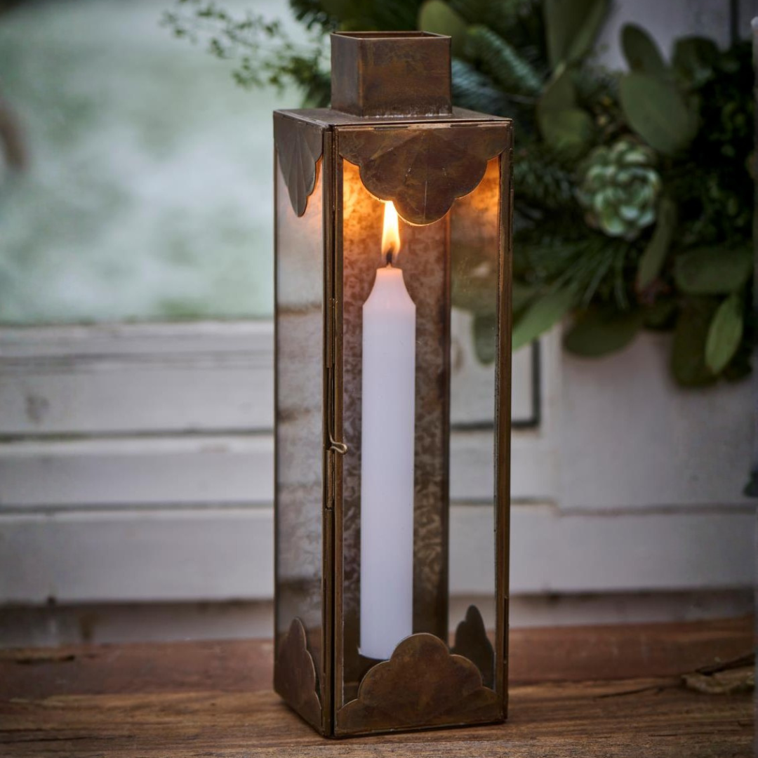 Høj firkantet lanterne i antik messing med glas og dekorativt udskåret metal med tændt hvidt lys