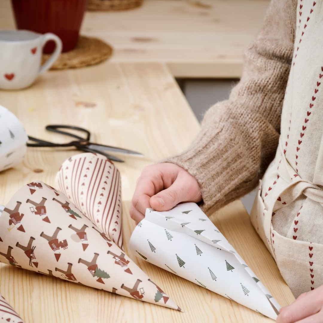 Beige gavepapir med røde striber og julemotiver, rullet til kegleformer på træbord