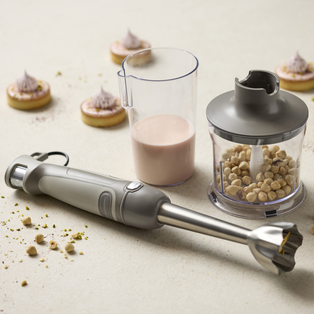 Latte-farvet stavblender med rustfrit stålhoved, gennemsigtigt målebæger og minihakker med nødder