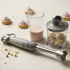 Latte-farvet stavblender med rustfrit stålhoved, gennemsigtigt målebæger og minihakker med nødder