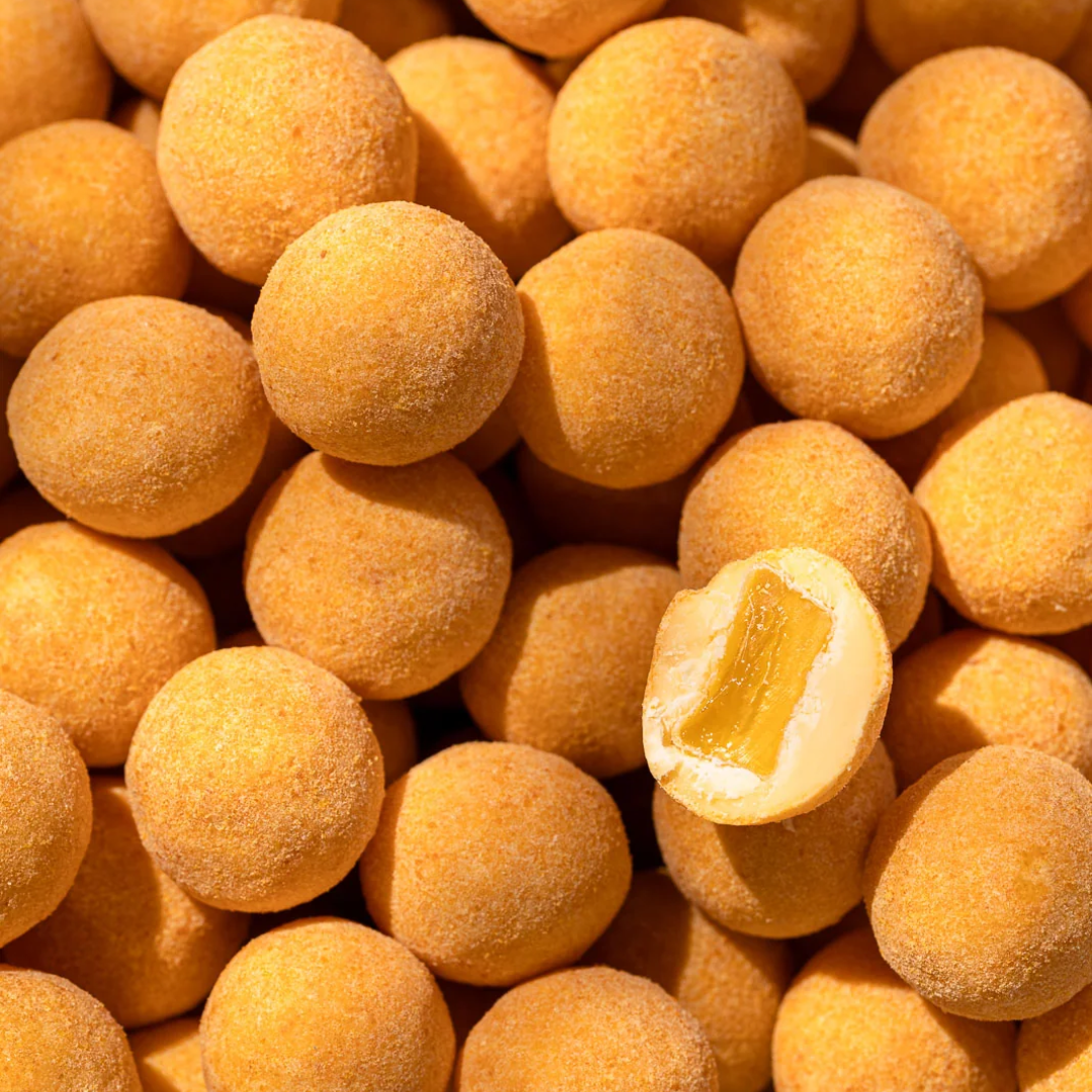 Gyldne chokoladetrøfler med mango-passionspulver, én halveret viser hvid chokolade og vingummi indeni