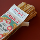 Gridelli Spaghettone pasta i hvid æske med grøn og rød etiket, tørre lyse spaghetti stikker ud