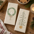 To pakker cremefarvede papirservietter med julemotiver: grankrans med lys og juletræ i potte