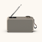 Kompakt DAB+ radio i beige med perforeret front, udtræksantenne og brun bærerem