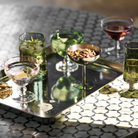Rektangulært serveringsfad i blank kromfinish med afrundede hjørner og glas med drinks