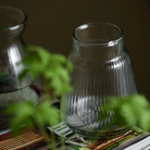 Klar glasvase med lodret riflet mønster og bred bund der smalner mod toppen