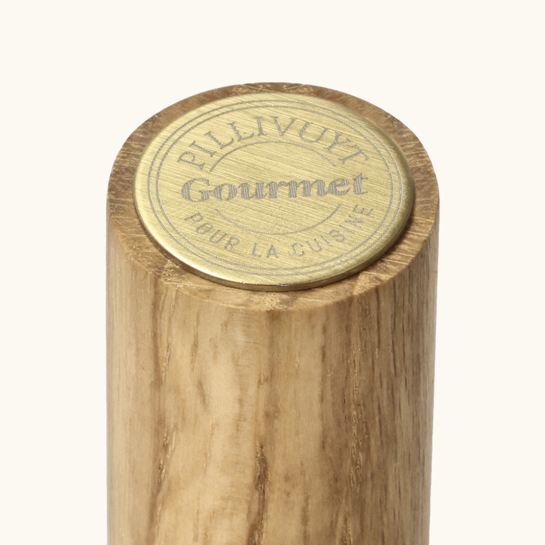 Nærbillede af toppen på køkkenrulleholder i lyst egetræ med messingfarvet Pillivuyt Gourmet-emblem